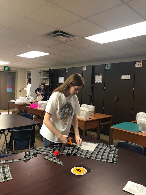 Students cuts through a plaid fabric for her smock.