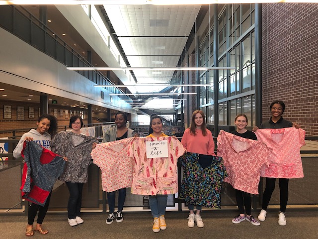 Fashion design students stand next to each other holding the smocks they created.